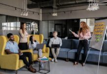 Managing Team Culture When Your Company Expands to a New City A diverse group of coworkers listens to a colleague presenting ideas on a whiteboard.