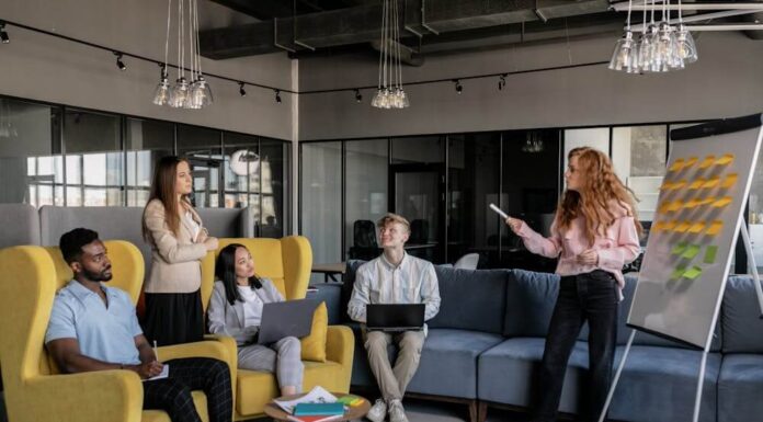 Managing Team Culture When Your Company Expands to a New City A diverse group of coworkers listens to a colleague presenting ideas on a whiteboard.